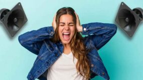 Girl with speakers on each side of her head holding her hands over her ears and looking distressed