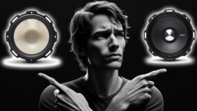 A confused looking man with his arms crossed pointing to two different types of speakers